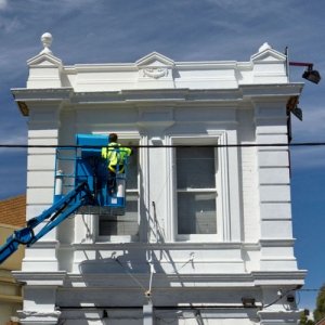 Painter applying external white paint on a building from a boom lift